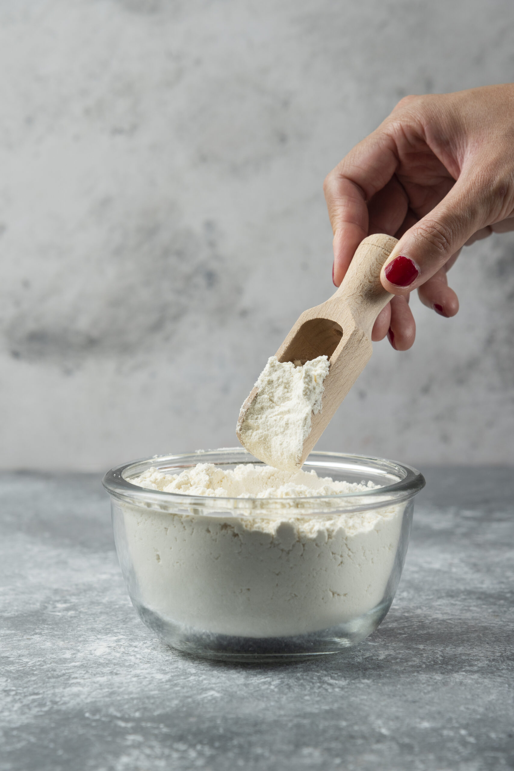 Woman hand holding spoon on top of flour bowl. High quality photo